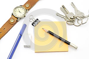 Orange post it with keys watch and bulldog clip and black pencil