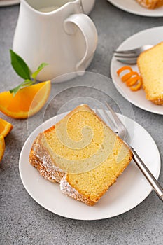 Orange pound cake slice on a plate, bundt cake topped with powdered sugar