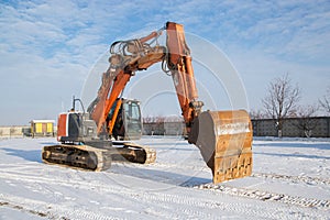 Orange powerful crawler excavator on the snowy ground of construction site