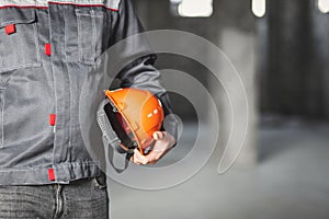 Orange protection helmet is in the hands of a construction worker in overall, copy space, construction site safety