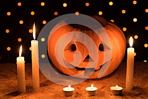 Orange pumpkin as a head with carved eyes and a smile with candles on a black background with a garland to the Halloween party