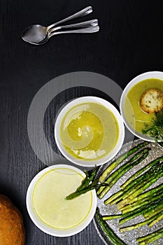 Orange pumpkin and asparagus soup in plates with cream on wooden background. Top view