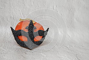 Orange pumpkin in black mask on light background