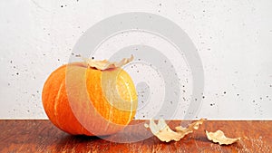 Orange pumpkin and dry oak leaves on brown wooden table on gray concrete wall background. Copy space, autumn composition