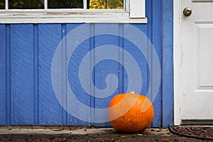 An orange pumpkin on the front porch of a purple house.