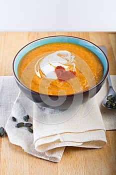 An orange pumpkin soup in a bowl on a linen cloth with pumpkin seeds and a spoon