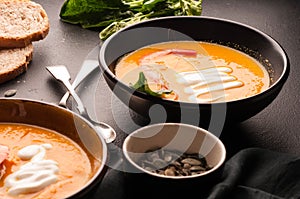 Orange pumpkin soup with shrimps, pumpkin seeds in dark bowls and bread, silver spoons