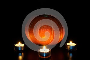 Orange pumpkin and three burned tea candles on black background. Halloween concept