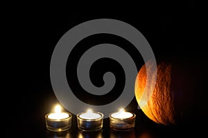 Orange pumpkin and three burned tea candles on black background. Halloween concept, copy space