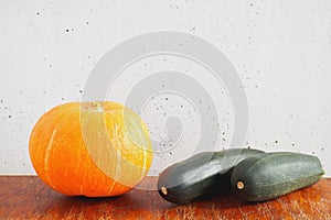 Orange pumpkin and two dark green zucchini on wooden table on gray concrete wall background. Copy space