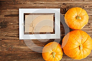 Orange Pumpkins with white frame for picture and brown paper package tied up with strings inside over wooden background