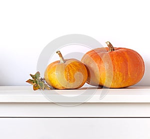 Orange pumpkins on the white wooden chest of drawers. Thanksgiving or Halloween festive concept decoration