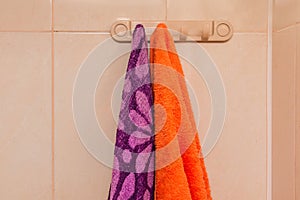 Orange and purple towels hanging on a hanger with hooks in the bathroom. Care and hygiene concept
