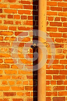 Orange or red brick stone wall with vertical rain gutter pipe metal in late afternoon or early morning sunrise in city