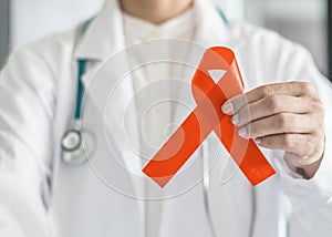 Orange ribbon for raising awareness on Leukemia, Kidney cancer, RDS multiple sclerosis, ADHD illness in doctor`s hand