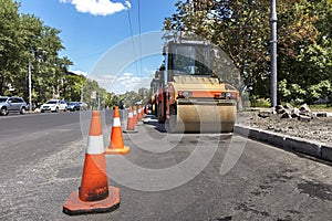 Orange road cones protect heavy wheel compactors along the edge of the city street road