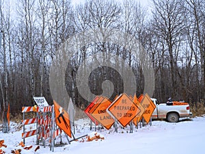 Orange Road Warning Signs stand in winter snow, near a Pilot Car pickup