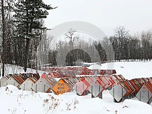 Orange ROAD WORK AHEAD sign among dozens of road signs in a snowy lot