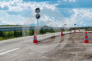 Orange road work cones, indicators on damaged  asphalt road