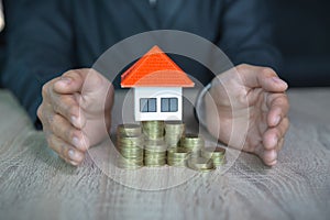 Orange roof house. Put on a pile of many coins. Home insurance concept of property protection A businessman protects an orange