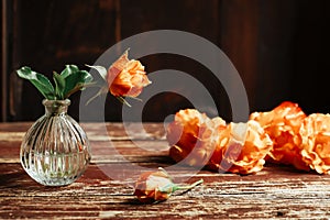 Orange roses in the vase and on the old wooden table