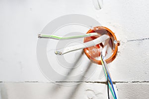Orange, round junction box mounted in the white wall with protruding electric cables.