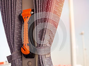 Orange safety hammer mounting near the window glass and curtain on the bus