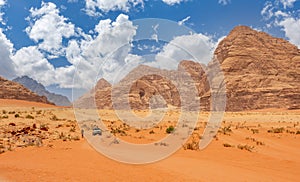 Orange sands and cliffs of Wadi Rum desert with tourist car in background, Jordan