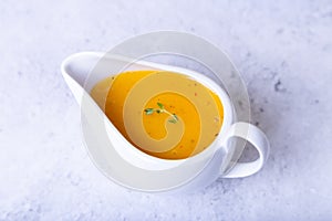 Orange sauce for duck poultry in a white gravy boat.