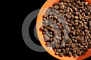 Orange saucer with coffee beans on black background