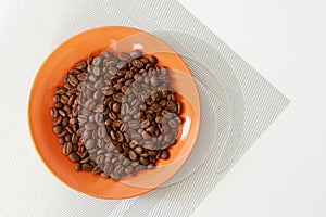 Orange saucer with coffee beans on white table