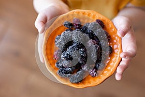 Orange saucer with frozen mulberries in children's hands