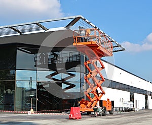 Orange scissor lift, a type of aerial platform, at work on a commercial building facade