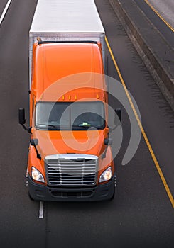 Orange semi truck with dry van trailer on the road top view