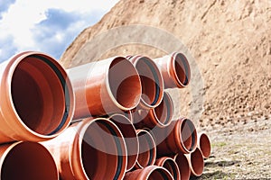 Orange sewer pipes at the construction site against the background of sand and blue sky. Preparation for the installation of an