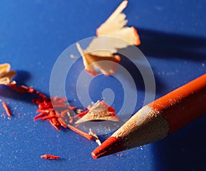 Orange sharpened colored pencil on blue background with wood shavings