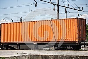 Orange shipping container mounted on a freight rail wagon. The image illustrates rail cargo handling, containerized freight and