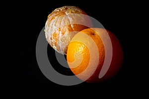 Orange with the skin and peeled orange together on black background