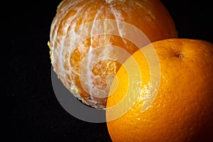 Orange with the skin and peeled orange together on black background