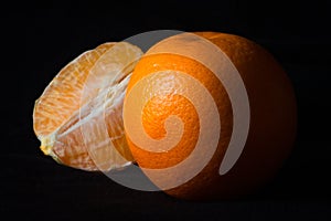 Orange with the skin and peeled orange together on black background