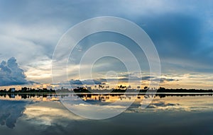 The orange sky, blue sky with the light of the sunset is above the city and river.