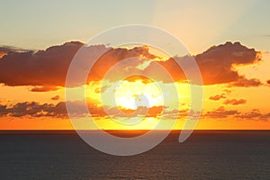 Orange sky with clouds over dark sea by sunrise