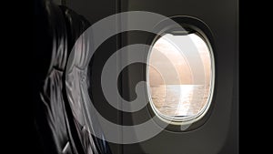 Orange sky reflect with sea ocean at sunset flare. View from window of passenger seat in cabin on commercial airplane.