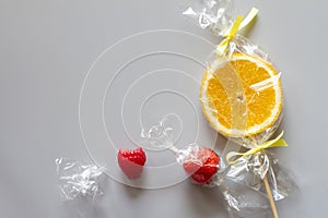 Orange slice on stick and fruits wrapped in foil, fruit lollipop, candies, healthy substitute for sweets, creative concept