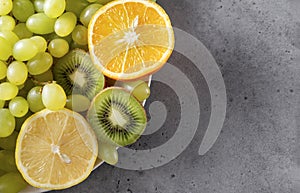 Orange slices, green grapes, kiwi, lemon slices on a gray background, fresh  fruit