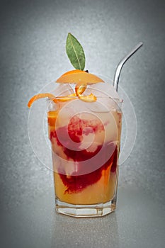 Orange slices, ice cubes and red syrup in a transparent cocktail glass, on glitter vignette background
