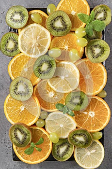 Orange slices, lemon, mint, sprig , green grapes, kiwi, on a grey background ,fresh citrus and fruit
