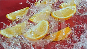 Orange slices splashing in water on red background. Citrus freshness. Pabulum. photo