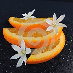 Orange slices with water drops and flowers on a black background