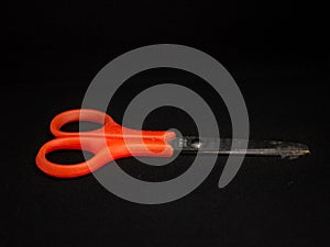 An orange small scissors from top view in black isolated background